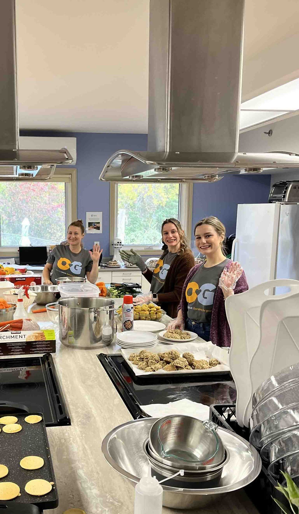 an image of three Organigram team members waving and smiling at the camera volunteering at a local food kitchen