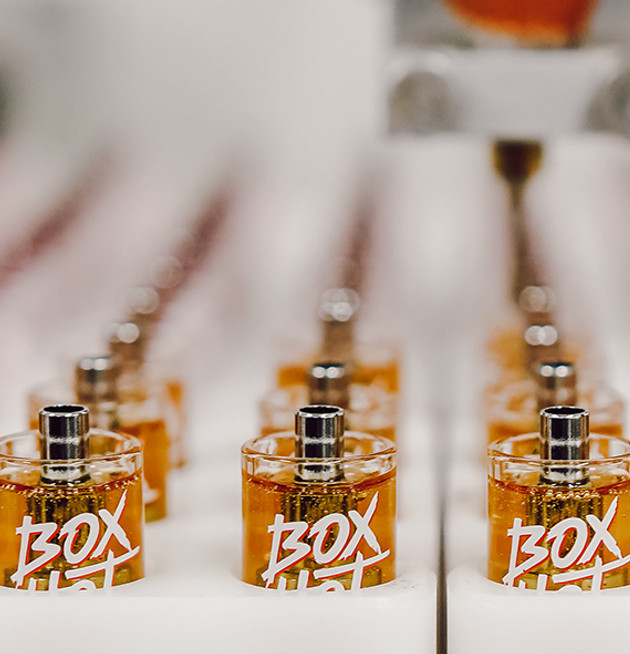 A close up photo of a number of Boxhot vape cartridges filled with oil, all upright in trays for inspection, the first row of carts is in focus and the following rows blur into the backgroud