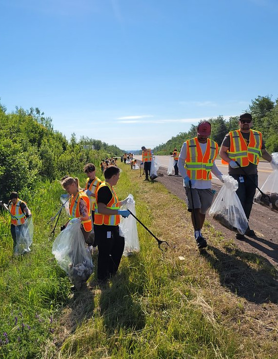 An outdoor photograph of more than a dozen Organigram team members taking part in a local cleanup effort, the team members are wearing safety vests and carrying garbage bags